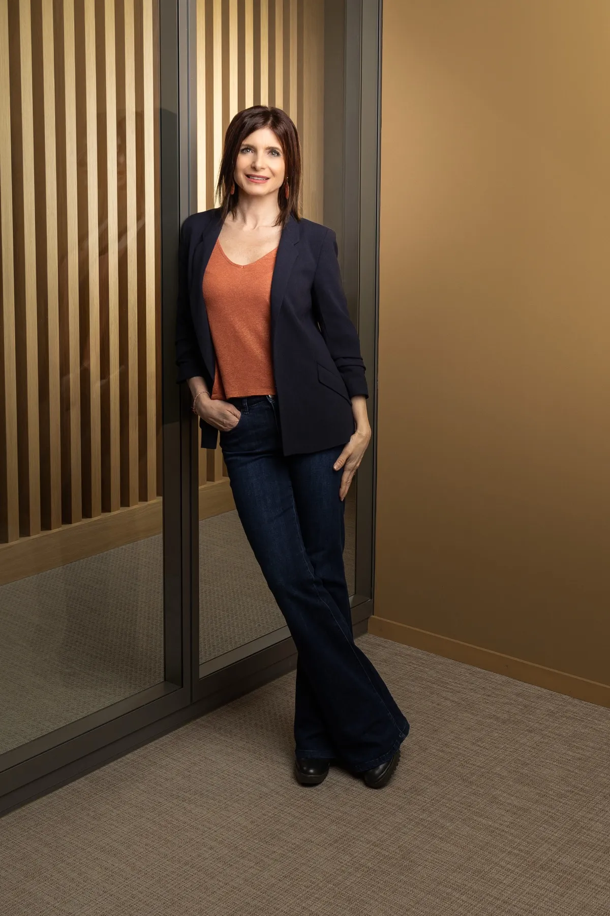 Véronique Pagano en pied, devant une cloison vitrée aux montants métalliques fins.